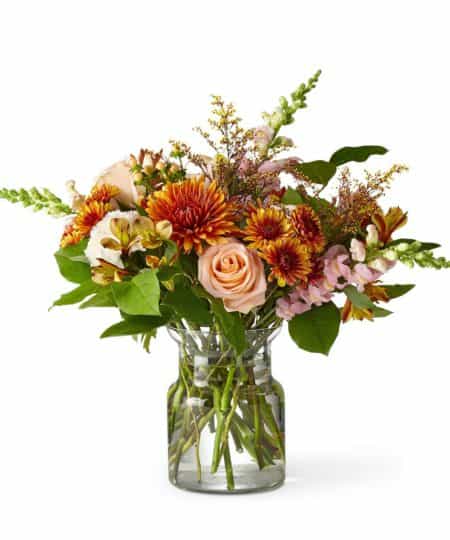 This is a gorgeous autumn bouquet combing burnt orange tones with delicate pink romantic touches. Flowers include varieties like roses, snapdragons and chrysanthemums with rustic solidago and greens.