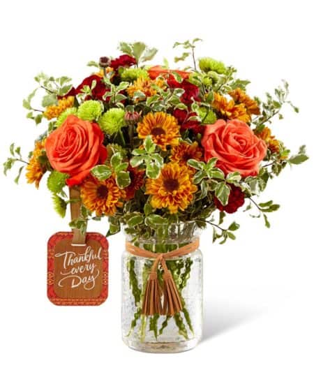 Our Many Thanks Bouquet makes a great gift idea to send during the Autumn months. Featuring orange roses and mums with burgundy mini carnations, green button poms and ample greenery. Please note that the exact vase shown is not available. Flowers will arrive arranged in a very similar glass mason jar vase. The "Thankful every Day" tag and tassel are available and are included as shown.